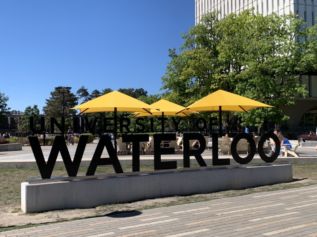 The Waterloo sign in the Arts Quad. You can see Dana Porter Library looming through the trees to the right and Modern Languages in the background.